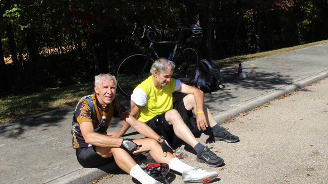 Two bicyclists sitting on a curb