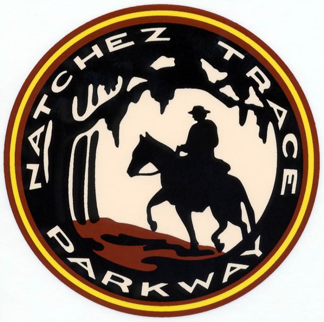 A circular logo with the text Natchez Trace Parkway following the edge of the circle. IN the center is a rider on a horse on a path through trees.