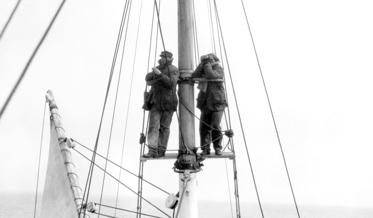 Two men stand at the crow's nest scanning for whales.
