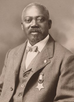 An older William Carney dressed in a suit with the medal pinned to his jacket.