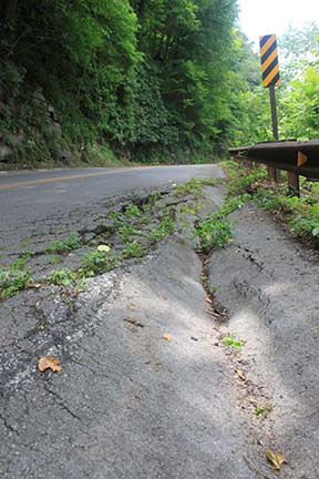 road with damaged area crumbling off side into woods