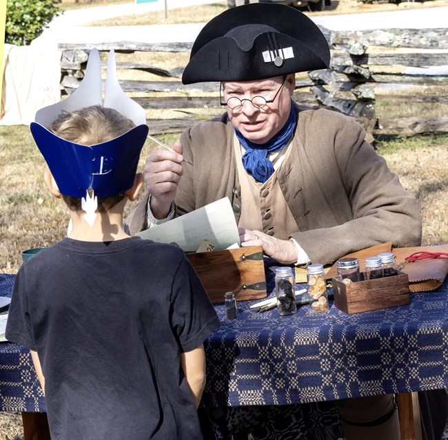 A man in 18th century clothing is speaking to a child.