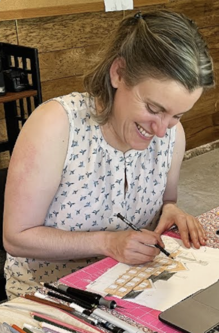 A blond woman at a table drawing.