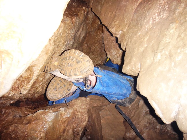 Feet of a caver in a small opening of the cave on the off trail section