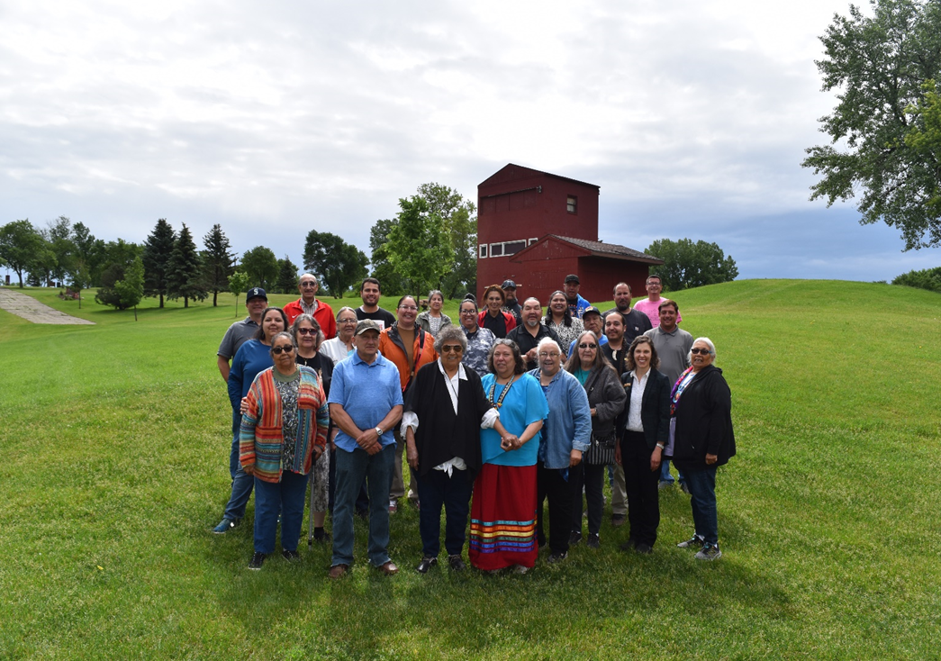 A large group of people standing together in a grassy field with a red barn in the background