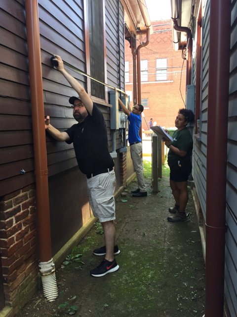 A group of people measuring the exterior of a building