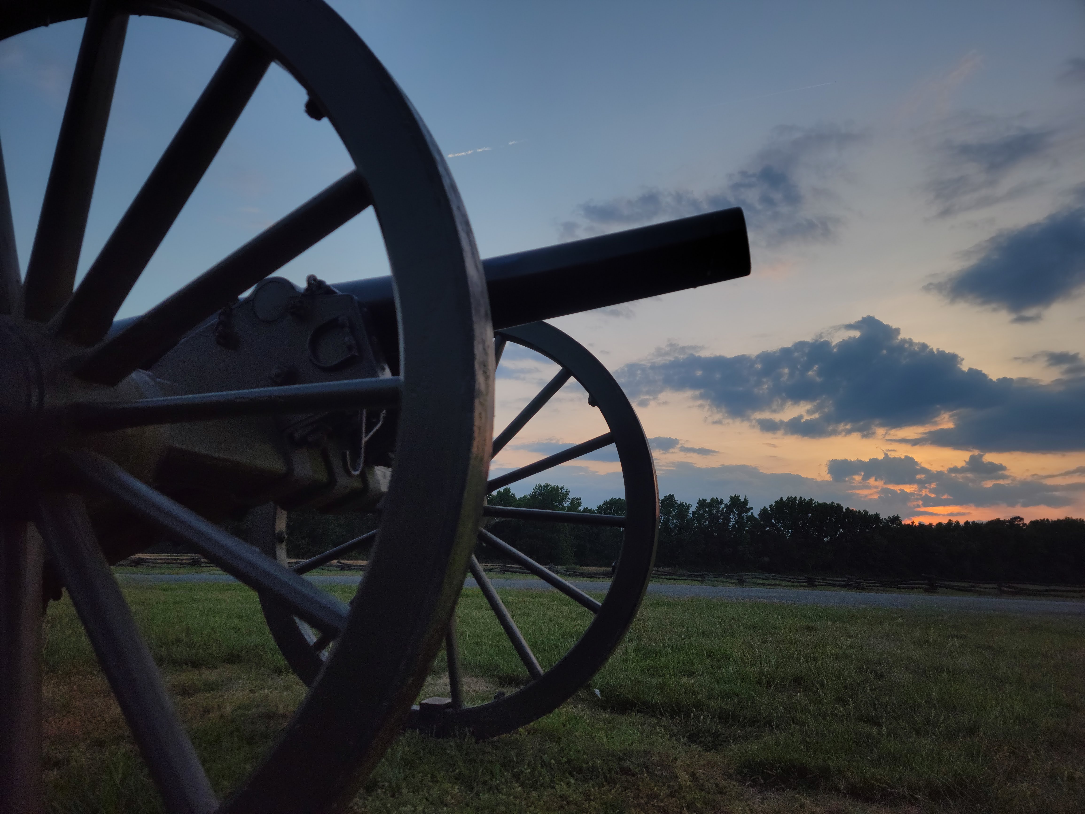 Morning light peaks through clouds over field viewed from ground level, closeup of cannon in foreground and overhead.