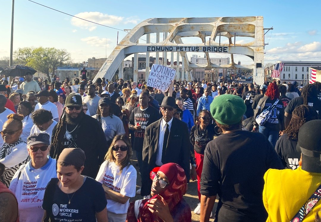 A large gathering of people walk across the Pettus Bridge.