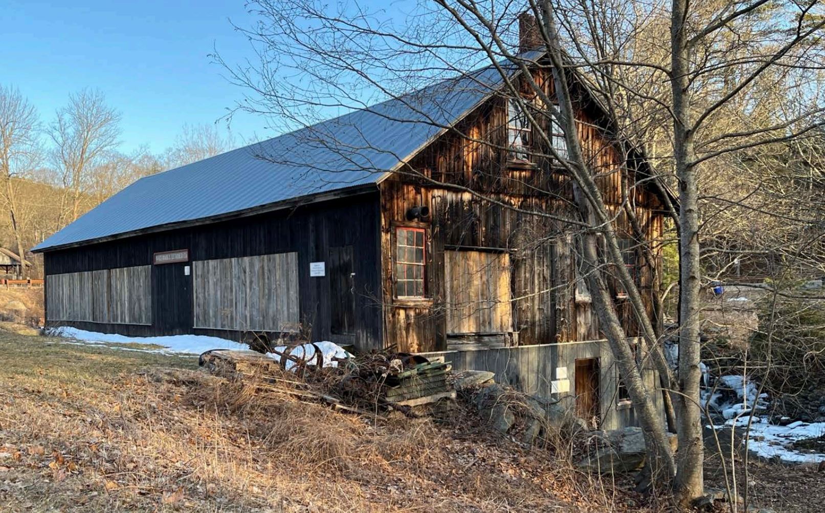 An old wooden building with a metal roof with a leafless tree in front of it.