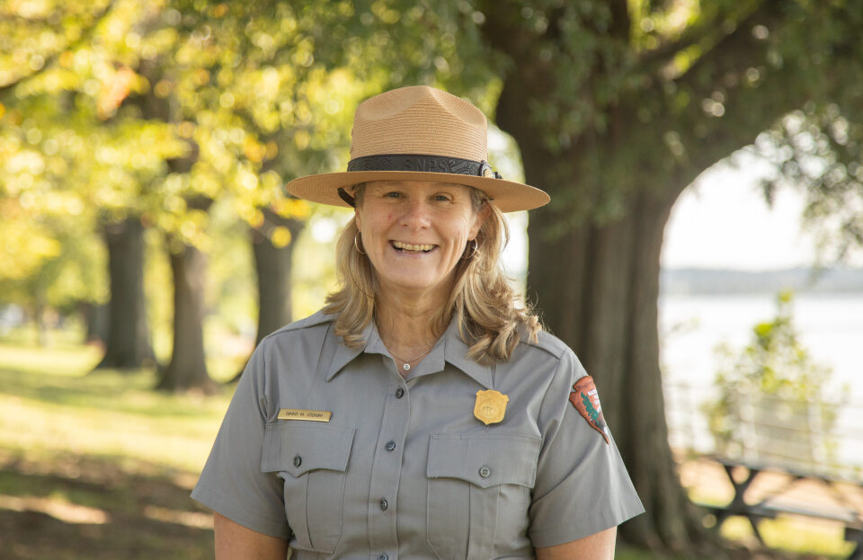 A woman in a National Park Service ranger uniform in front of trees.