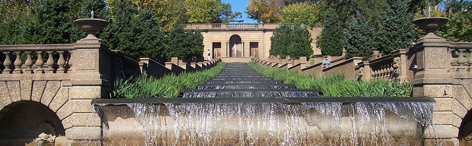 Water cascades over a stepped fountain, framed by concrete walkways, ledges, and walls.