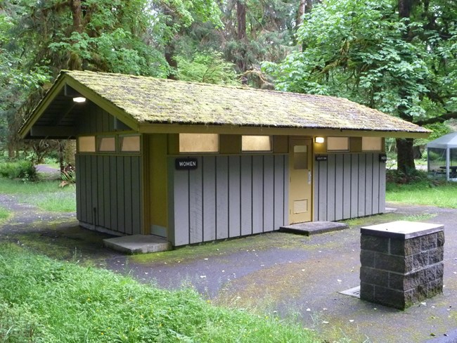 A one-story Mission 66-era wood paneled comfort station with a wood shake side-gabled roof