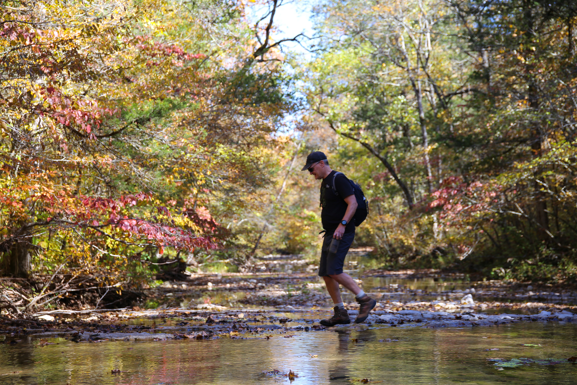 A man steps across a rocky creek in the fall.