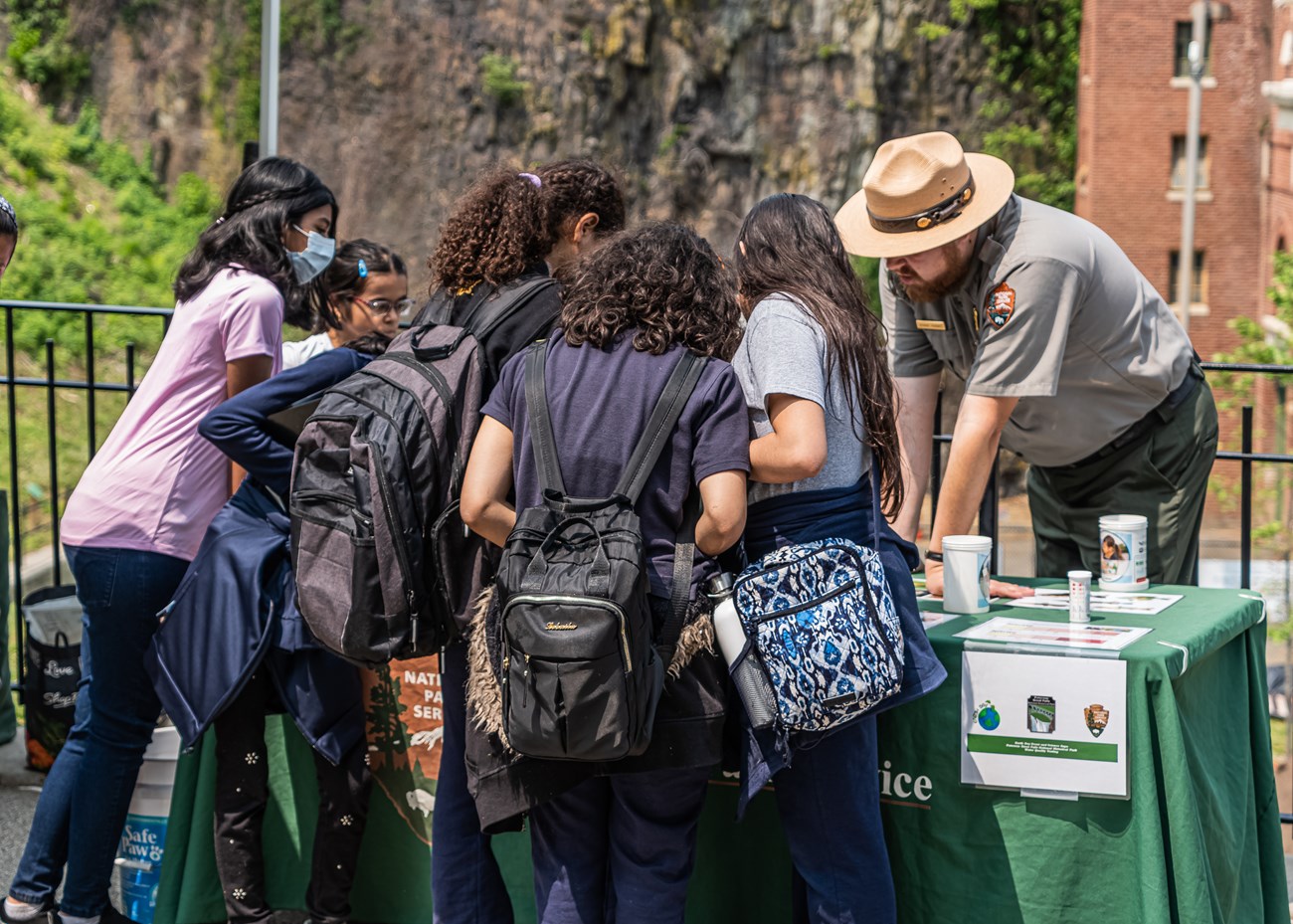 A park ranger leans over an activity table, working with a crowd of young students
