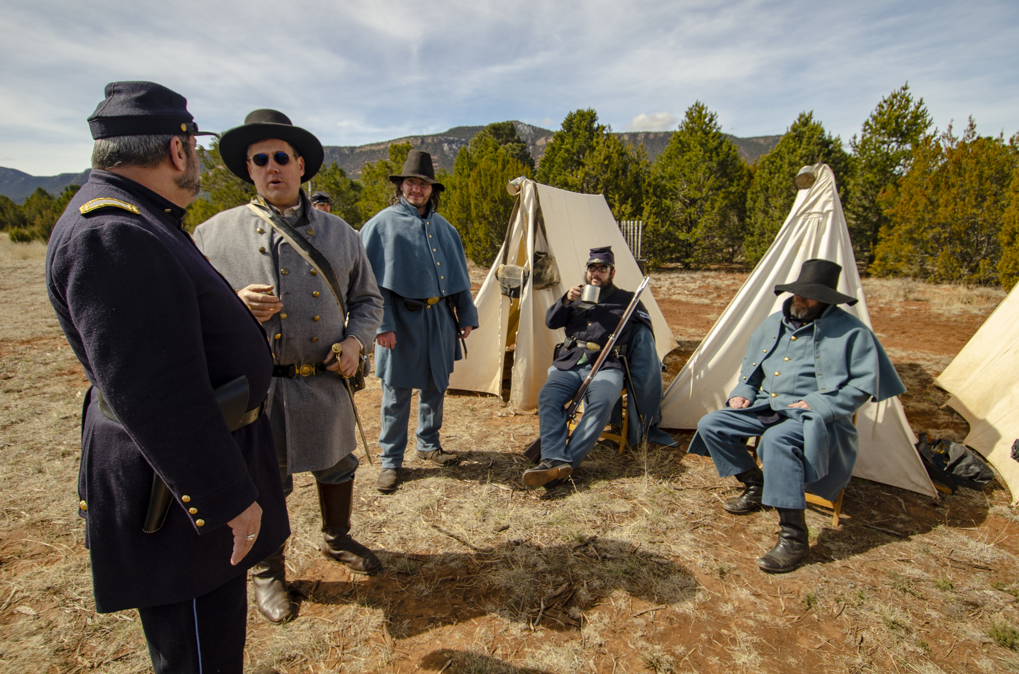 Men dressed in Civil War uniforms with canvas tents behind them.