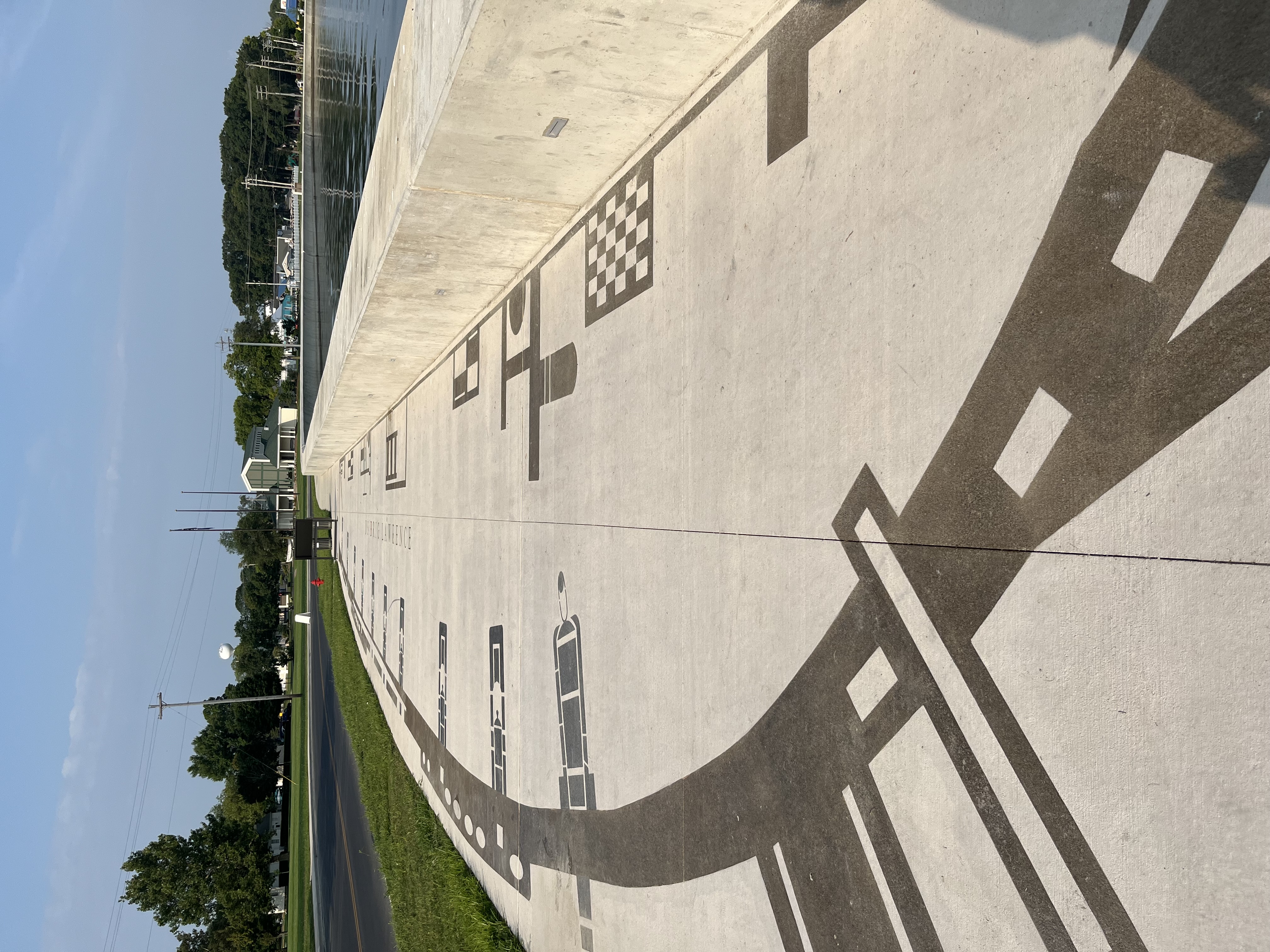 10 foot wide sidewalk along a seawall that rise 32 inches above sidewalk. Etched into sidewalk is the brown out line of a sailing ship and black of naval guns.