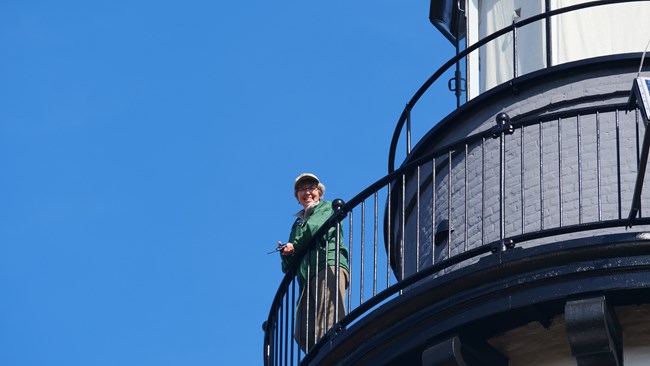 A person peeks out from the balcony of the Au Sable Light Station