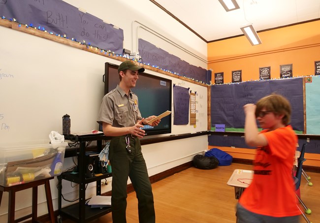 a student dances around a park ranger during a classroom visit