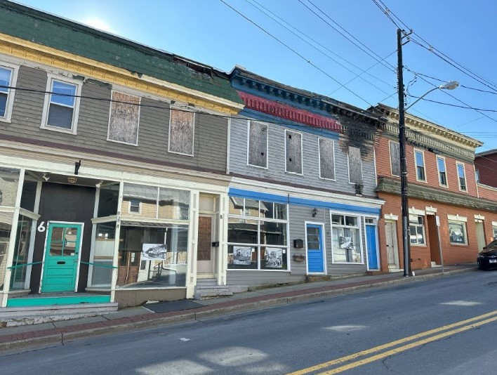 A row of three historic buildings line an inclined street.