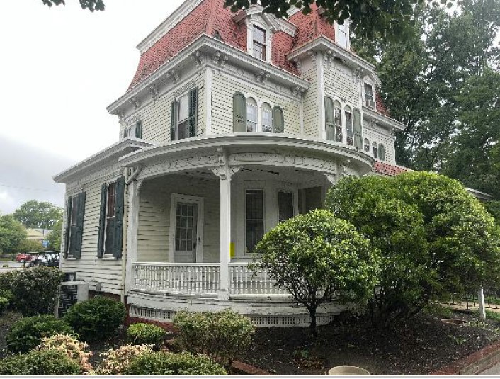 A pre-1885, three-story frame building with Queen Anne architectural features including a mansard roof and an expansive porch.