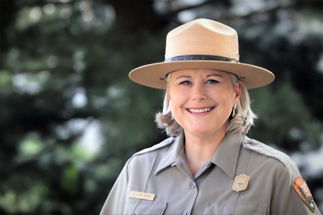 A middle-age woman with shoulder legth hair is wearing a ranger uniform and posing for camera.