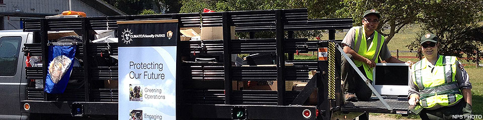 Two uniformed park employees loading electronic waste into a gray stake bed truck.