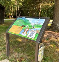Track trails sign at the edge of a sidewalk in a green forest