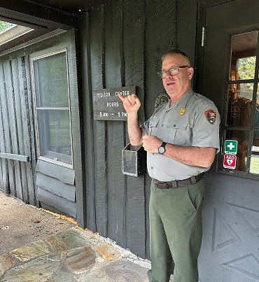 Park ranger standing in front of a wooden building talking with his hands (using sign language)
