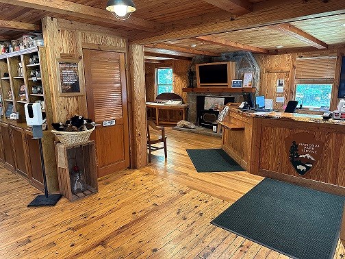 Interior of wood paneled visitor center with bookshelves of the store displays to the right and large wooden information desk with the NPS arrowhead to the left