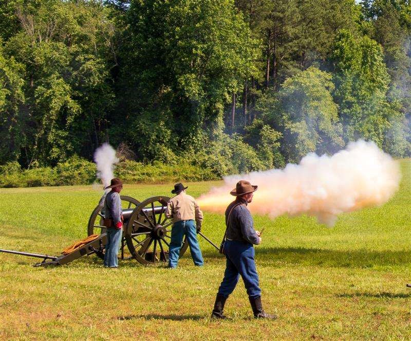 smoke and flame explodes from the barrel of a Civil War cannon manned by uniformed reenactors.