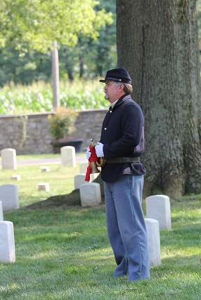 A Civil War Union soldier stands in a cemetery, holding a bugle