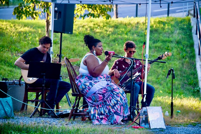 A woman sings into a microphone and two musicians play guitars
