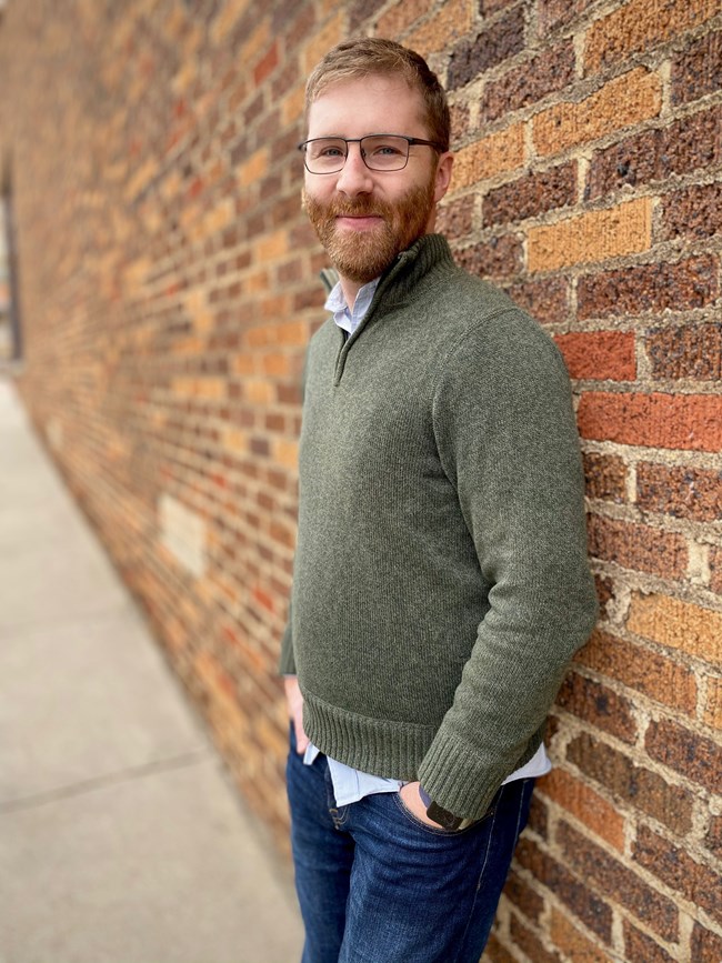 Headshot of RMNP's Artist-in-Residence Garrison Gerard, standing outside in front of a brick wall.