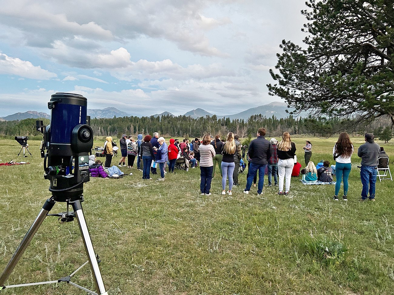 A group of over 100 people are gathered in a meadow for the program Astronomy in the Park