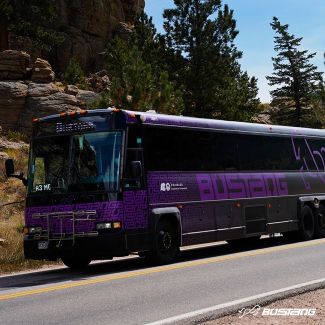 A Bustang coach bus is pictured driving on Bear Lake Road inside Rocky Mountain National Park