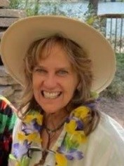 Photo of Deb Price, wearing a tan wide-brimmed hat and smiling while looking forward.