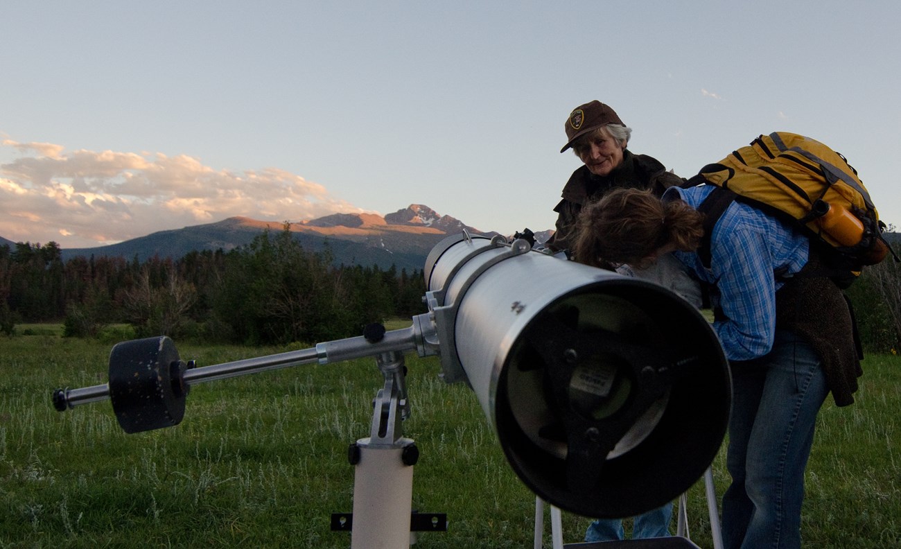 A park visitor is looking at features of the night sky through a telescope
