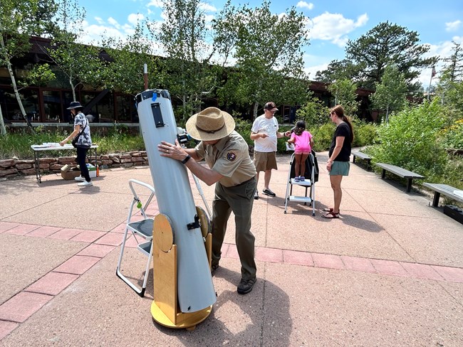 An NPS Volunteer is looking into a solar telescope and looking up at the sun