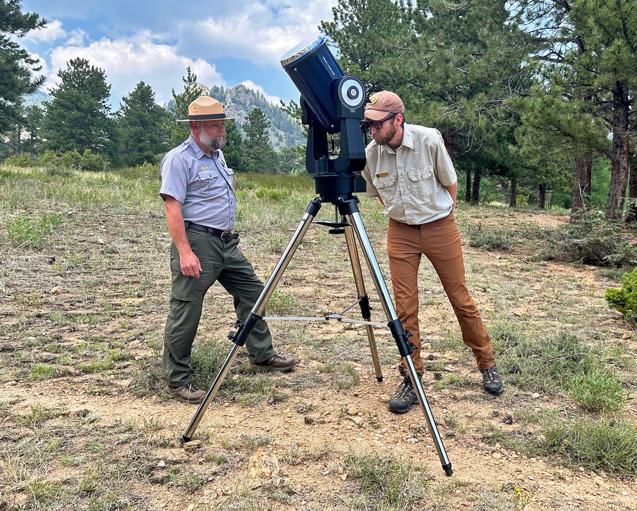 An NPS volunteer is looking through a Solar Telescope and a park ranger is standing next to them