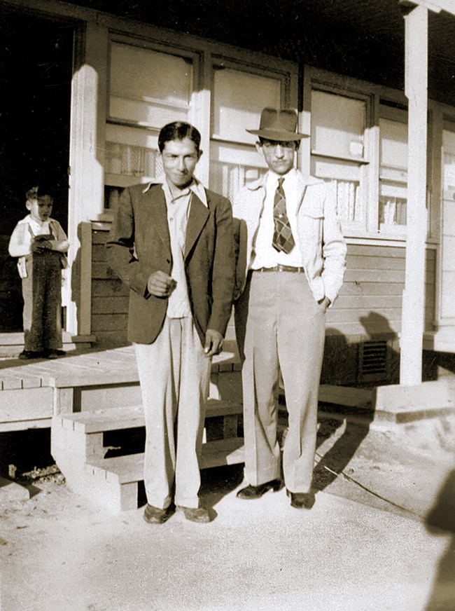 Two young latin men in suits are posting in front of a house.