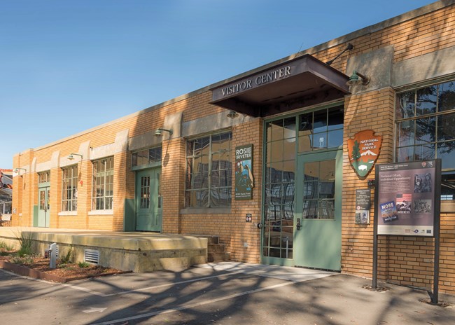 Photo of a brick building with multiple windows and a front door. Entrance to the visitor center.