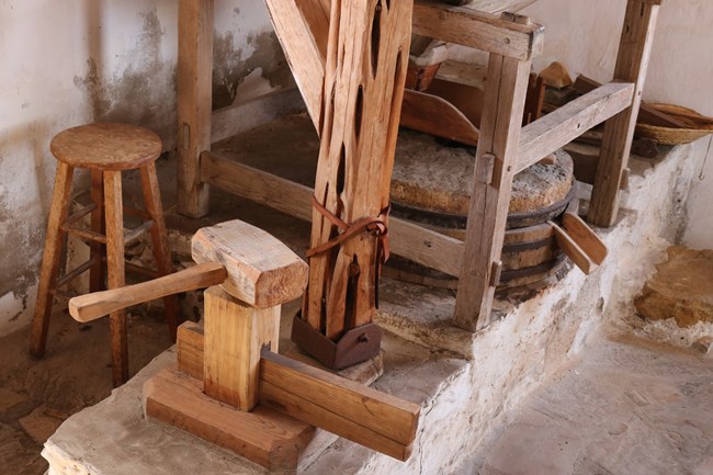 The interior of the gristmill building is a small stucco room with reconstructed milling equipment including two round millstones.