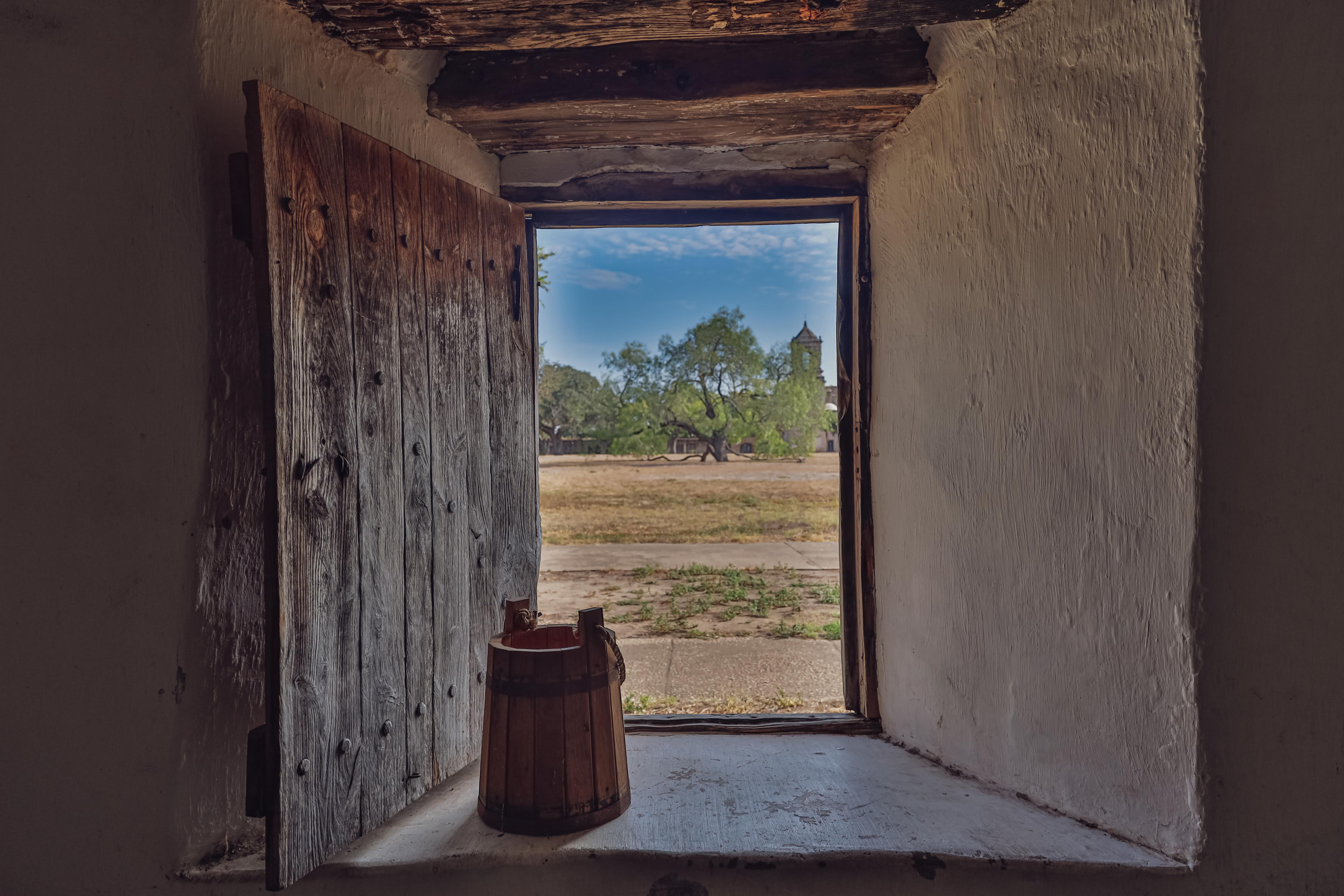 open window with a bucket and a view of a grassy area ahead