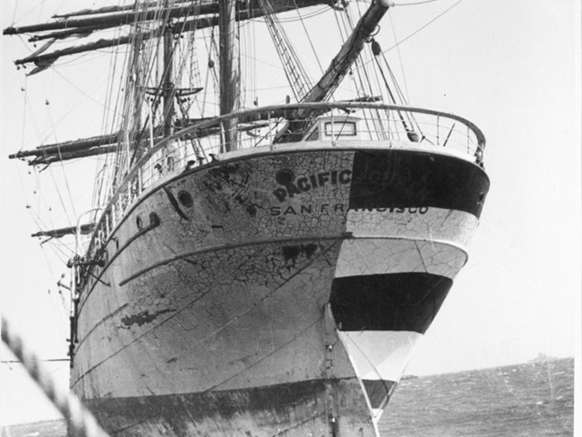 historical photo of the Pacific Queen, viewed from the stern, showing one half of the hull painted for use on a movie set