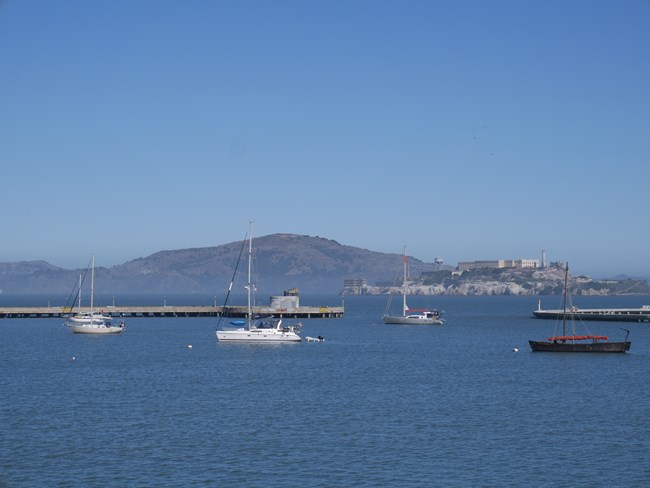 sailboats sit anchored in Aquatic Park Cove, with Alcatraz Island visible in the background.