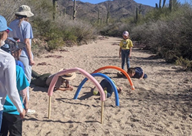 kids crawl under archways made of pool noodles in a desert wash