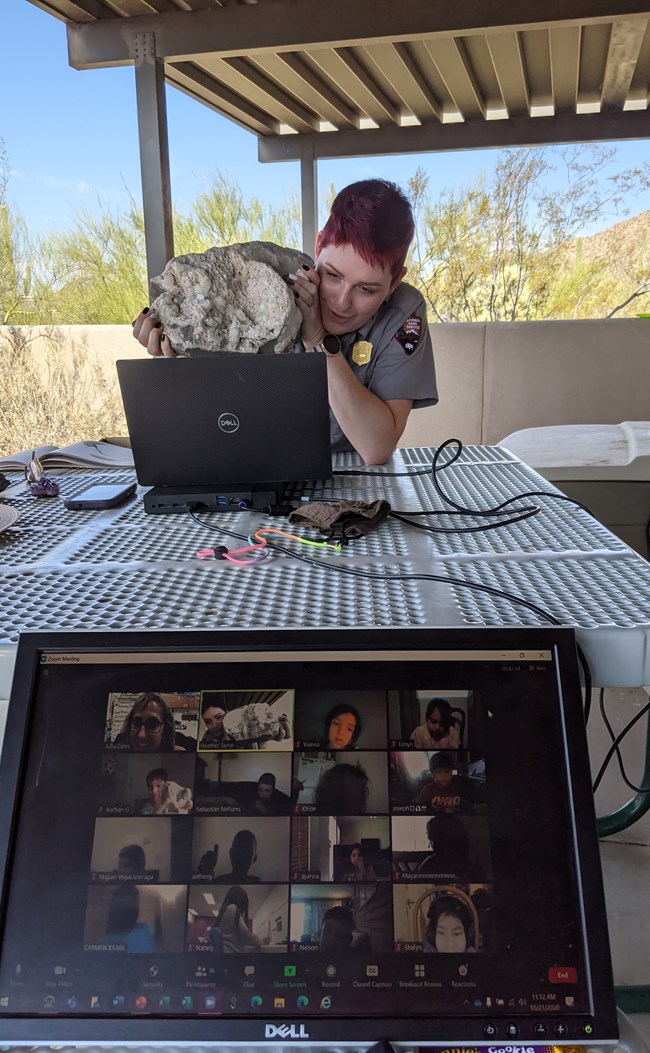 ranger holding up artifact in front of computer screen, laptop displays video conference in progress