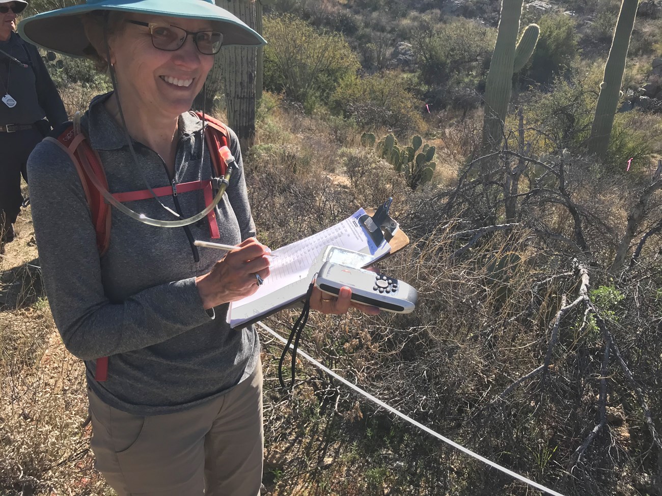 A volunteer smiling. She is holding a GPS device and a clipboard with the data sheets.