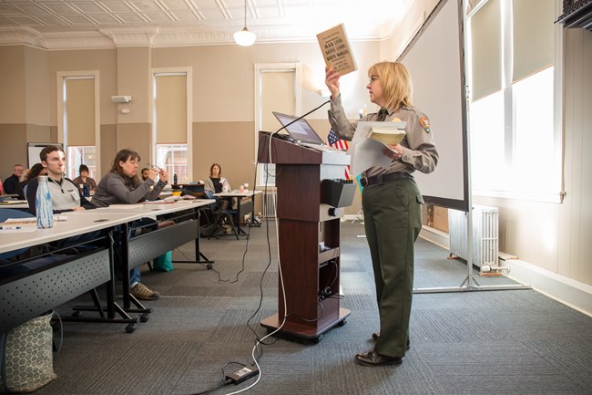 Female park ranger standing at podium and holding up a book.
