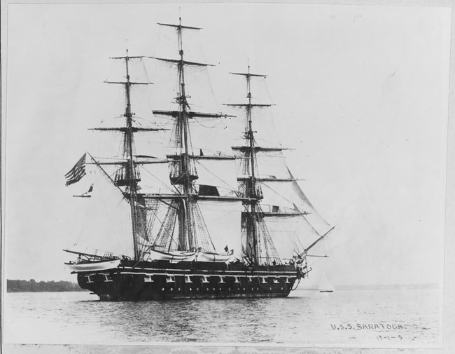 A black and white depiction of a big wooden ship with 14 sails sits on calm waters.
